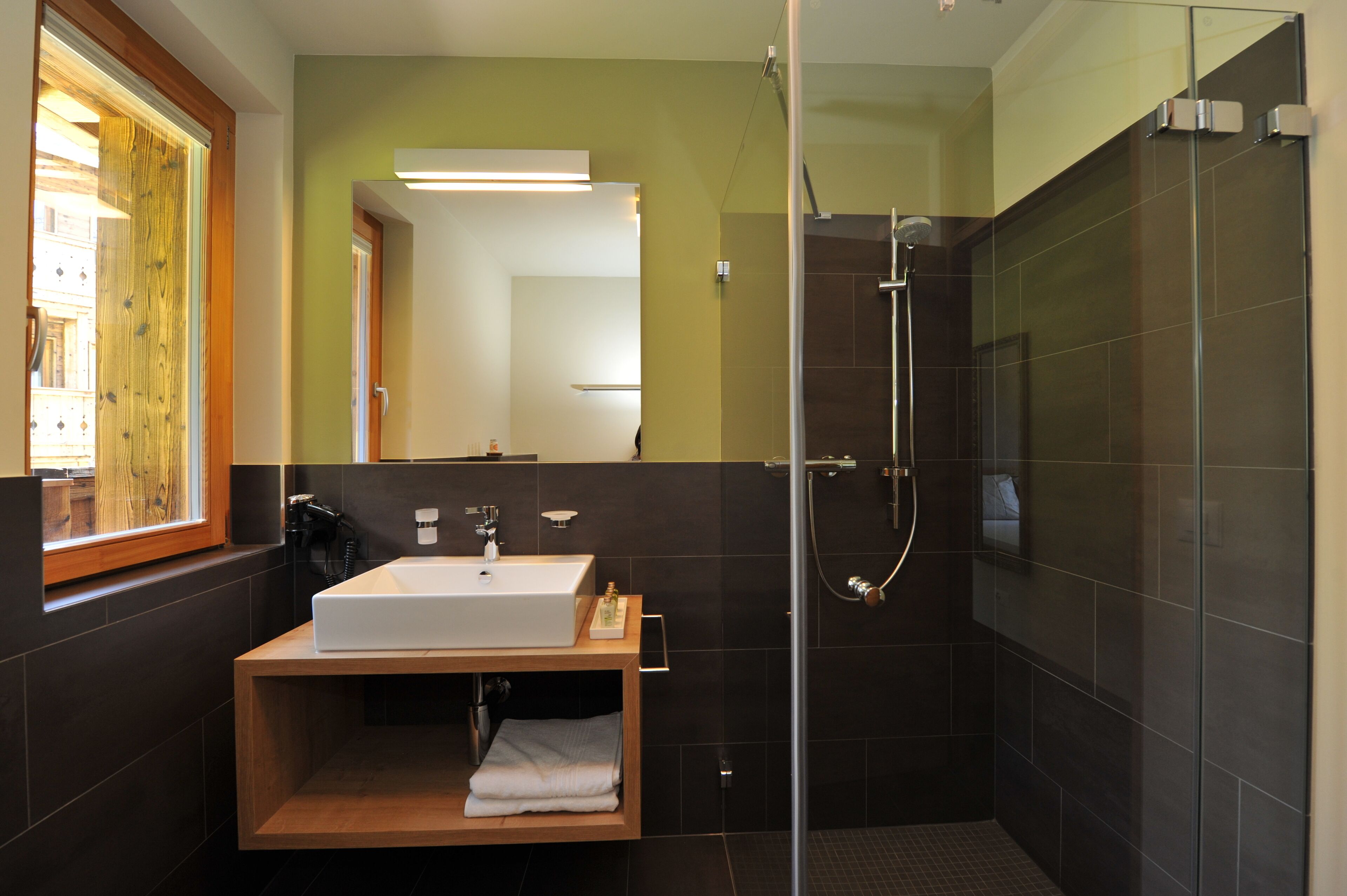 A modern bathroom with a glass-enclosed shower, a wooden vanity with a white sink, and a mirror above the sink.