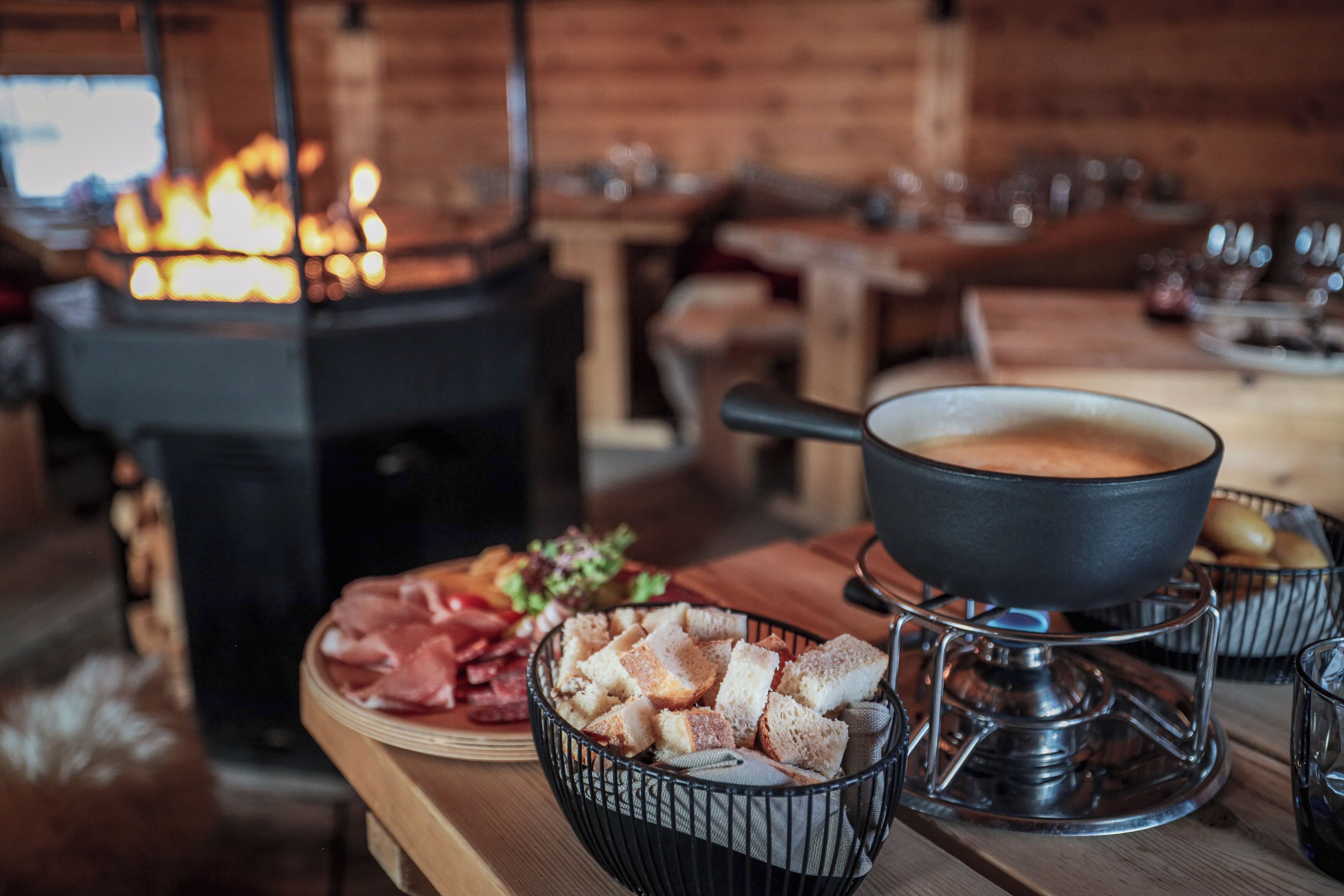 A dining table with a hot pot, bread, and charcuterie.