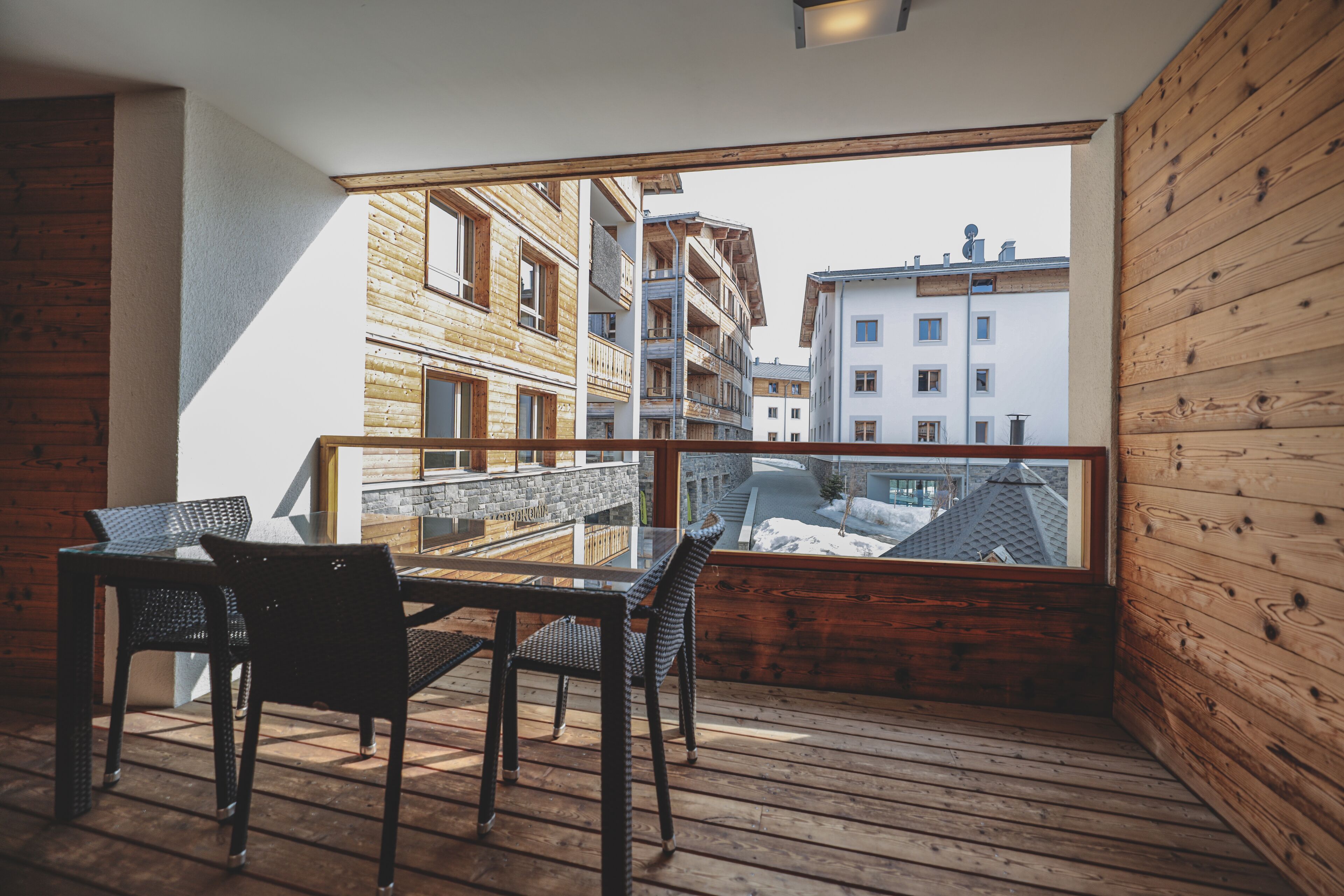 A balcony with a wooden floor, a glass table, and two chairs.