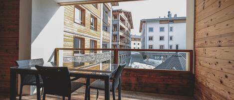 A balcony with a wooden floor, a glass table, and two chairs.