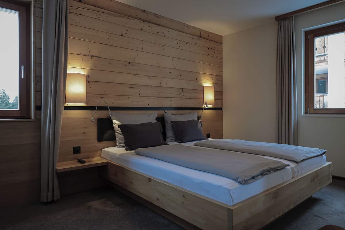 A wooden-paneled bedroom with a bed, bedside lamps, and a window.