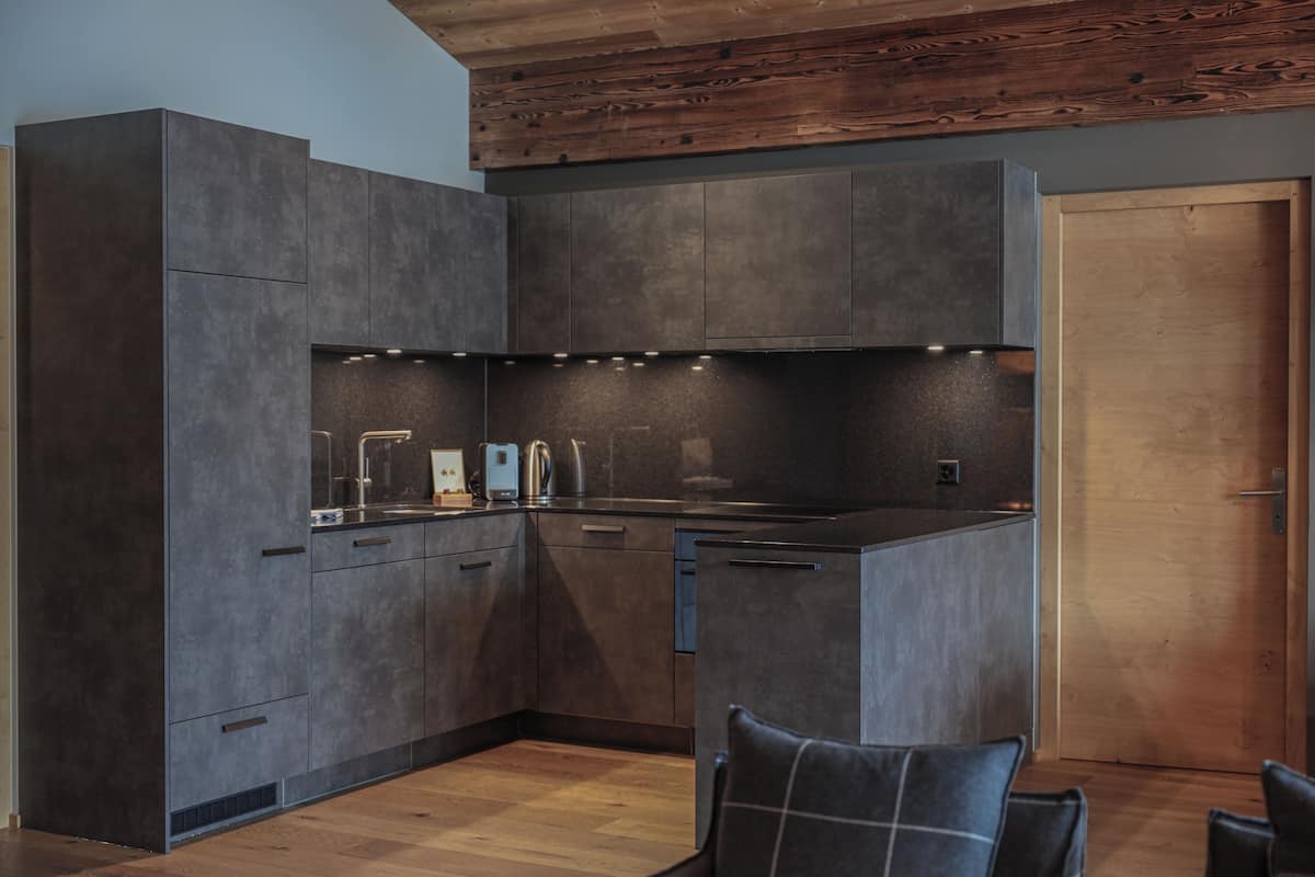 A modern kitchen with dark cabinetry, a built-in oven, and a wooden ceiling.