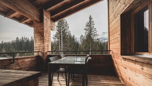 Terraza de madera con una mesa y sillas, con vista a una zona montañosa boscosa.