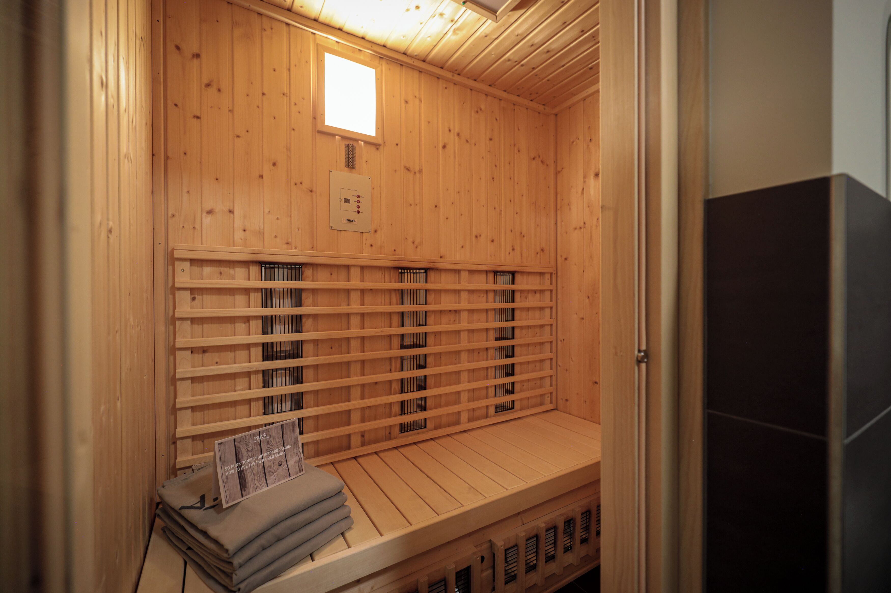A sauna with wooden walls and benches, a small window, and a control panel.