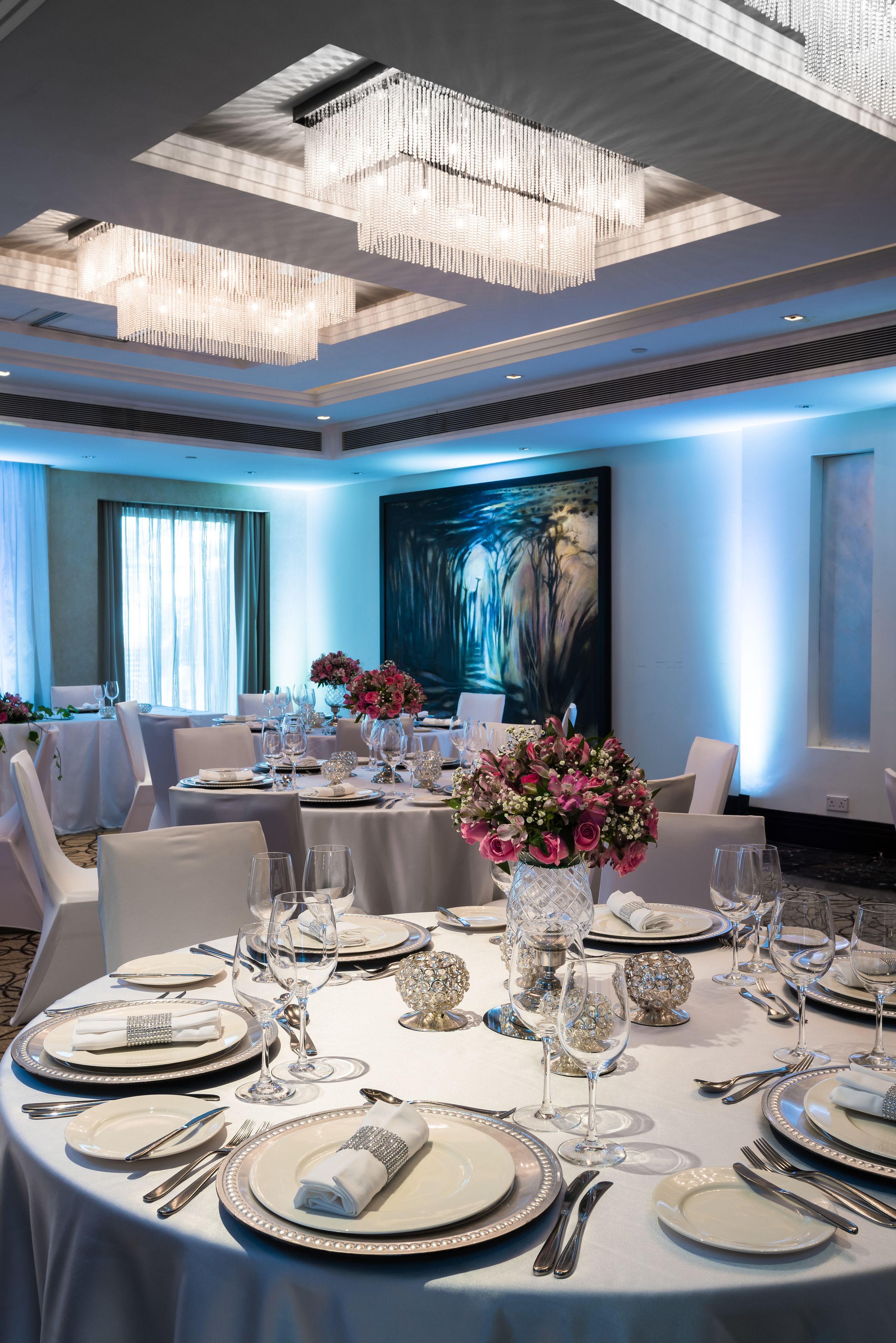 Una sala de conferencias bien iluminada con mesas redondas dispuestas para un evento formal, que presenta cristalería de cristal y centros de mesa florales.