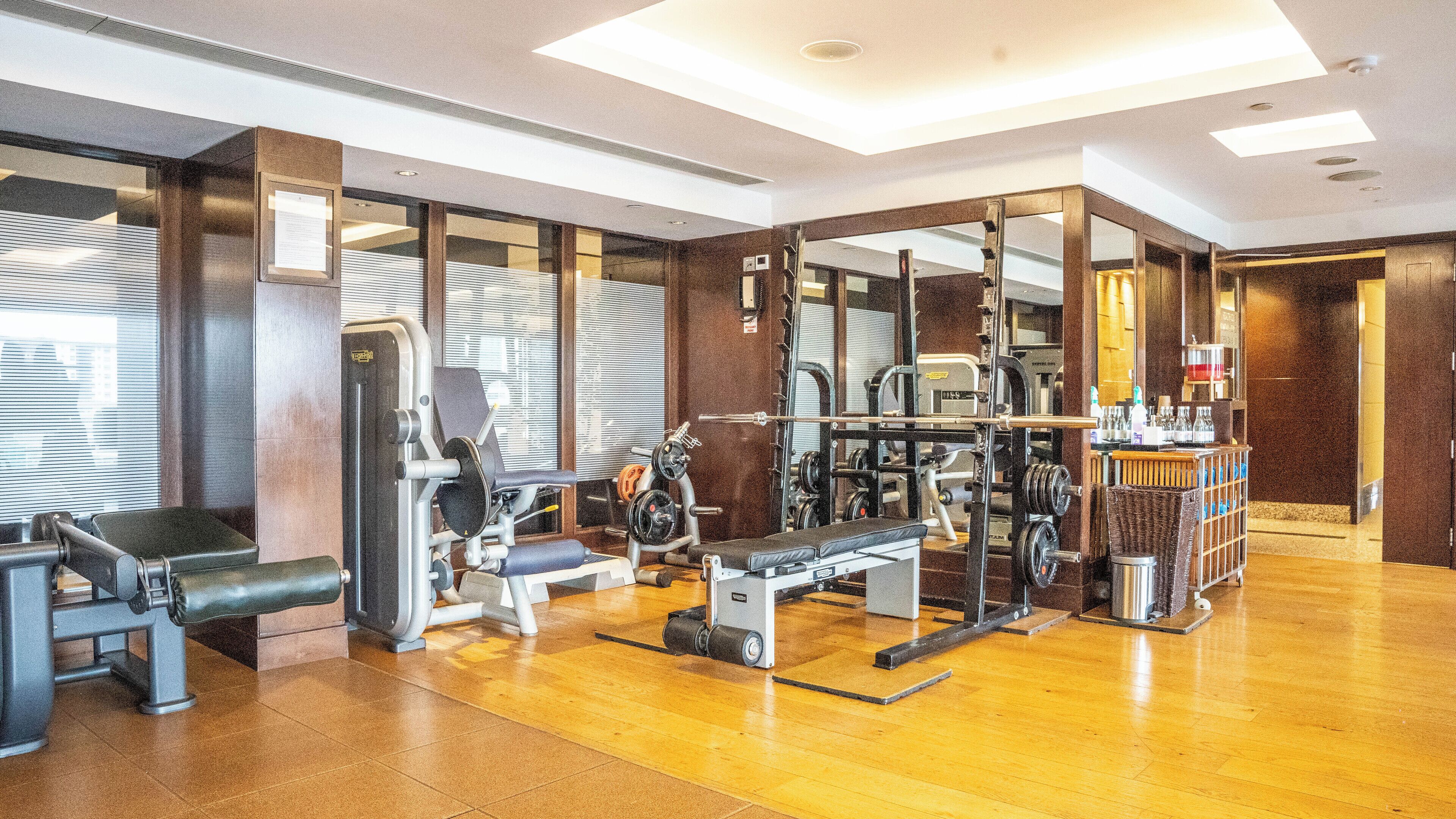 Une salle de sport équipée de divers appareils d’exercice, dotée d’un mur entièrement recouvert de miroirs et d’un plancher en bois.