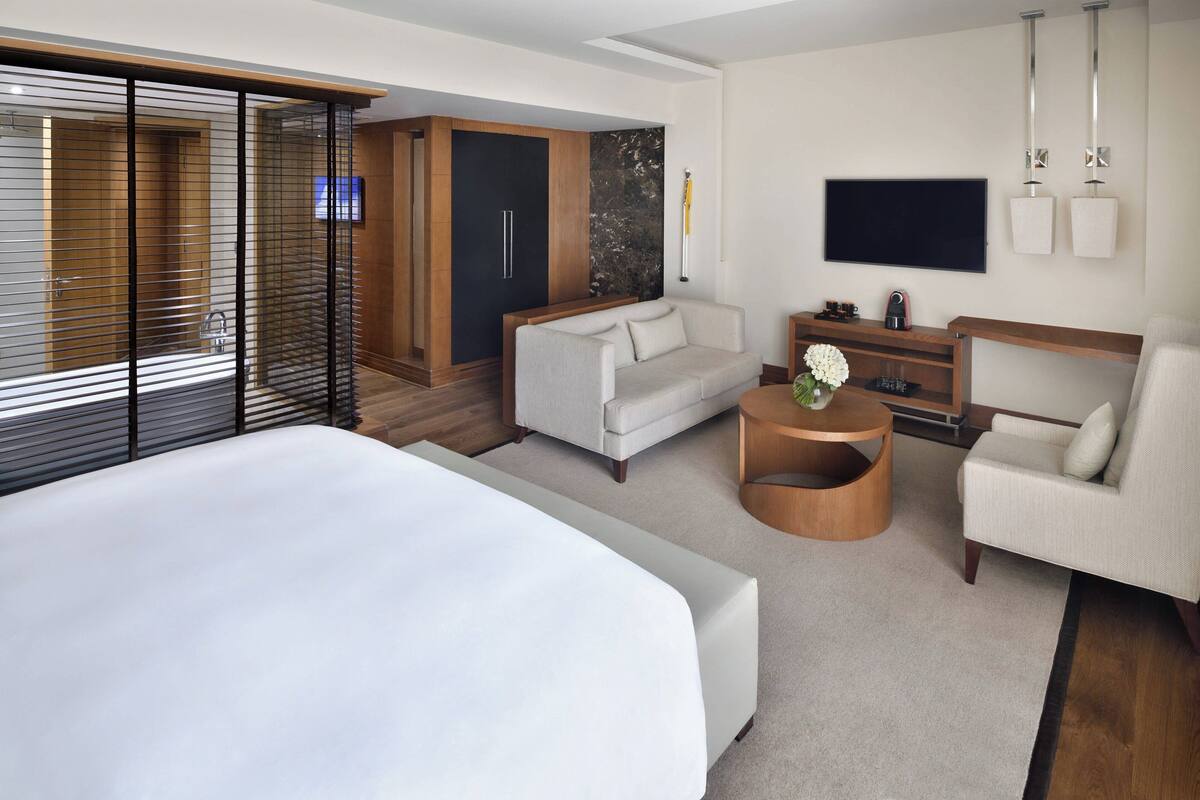 A modern hotel room with a large bed, a sofa, a TV, and a wooden cabinet.
