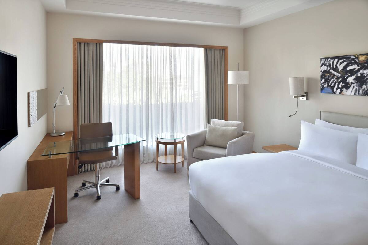 A hotel room with a large bed, a desk with a chair, a small round table, and a sofa.