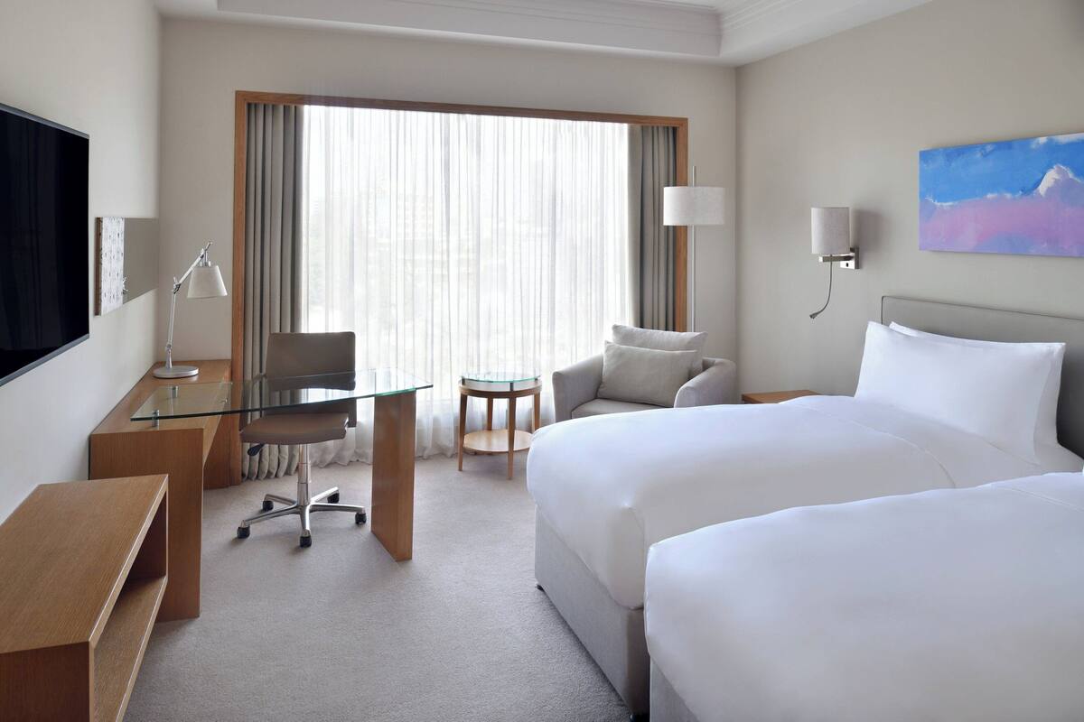A hotel room with a bed, a desk, a chair, a TV, and a painting on the wall.