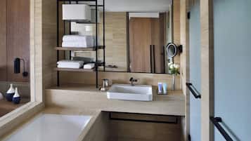 Un baño moderno con un espejo grande, lavamanos blanco y un estante empotrado con toallas.