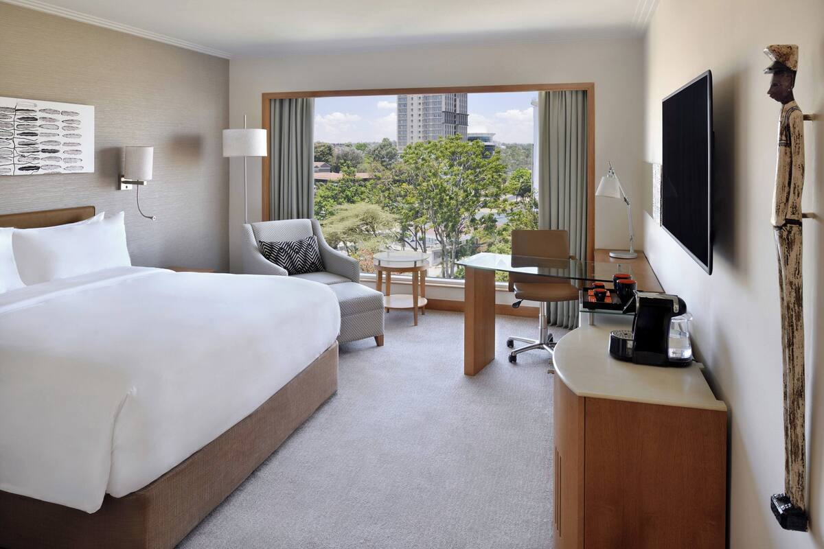 A hotel room with a large bed, a desk, a chair, a coffee maker, and a TV.