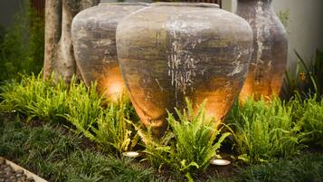 Three large glass vases with a rustic finish, placed on a bed of green ferns and surrounded by rocks.