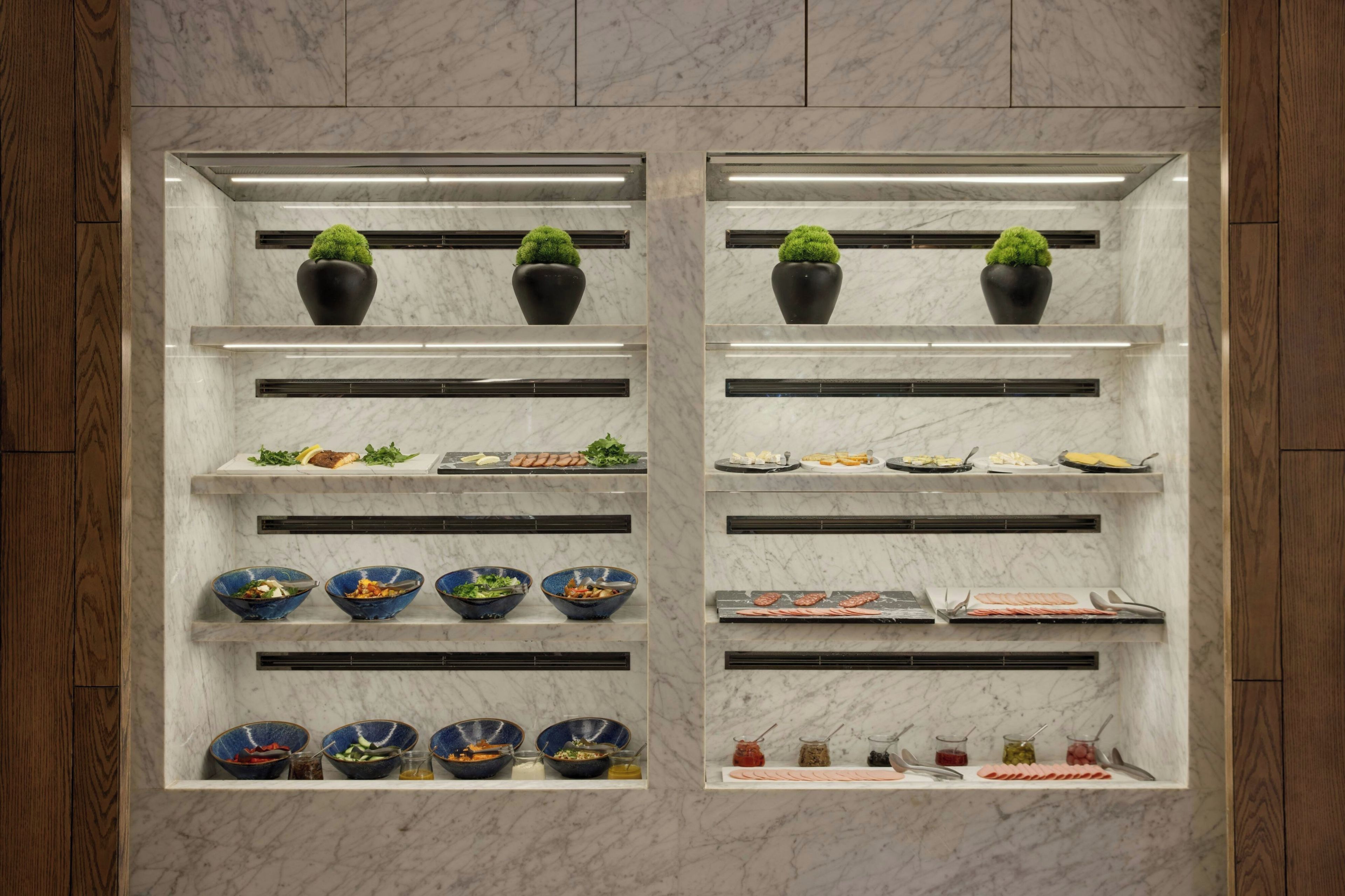 A kitchen with marble countertops, black pots with green plants, and various food items.