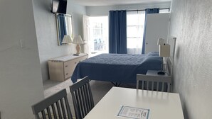 Ein Hotelzimmer mit Bett, Schreibtisch, Stuhl, Kommode, Spiegel und einem Fenster mit Vorhängen.