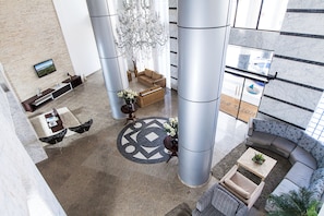 Un hall d’entrée spacieux au design moderne, comprenant un grand espace salon avec des canapés et des fauteuils, un tapis décoratif central et un téléviseur fixé au mur.