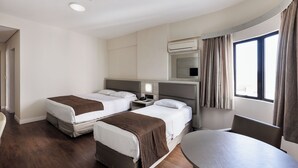 A hotel room with two beds, a desk, a chair, and a large window with curtains. - Hotel D Sintra (Balneário Camboriú)