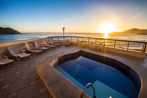 Un espace piscine avec des chaises longues et une vue sur le coucher de soleil sur l’océan.