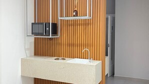 A modern kitchen with a built-in microwave, a sink, and a wooden panel wall. - Hotel D Sintra (Balneário Camboriú)