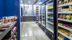 A grocery store aisle with refrigerated sections and shelves stocked with snacks and beverages. - Hotel D Sintra (Balneário Camboriú)