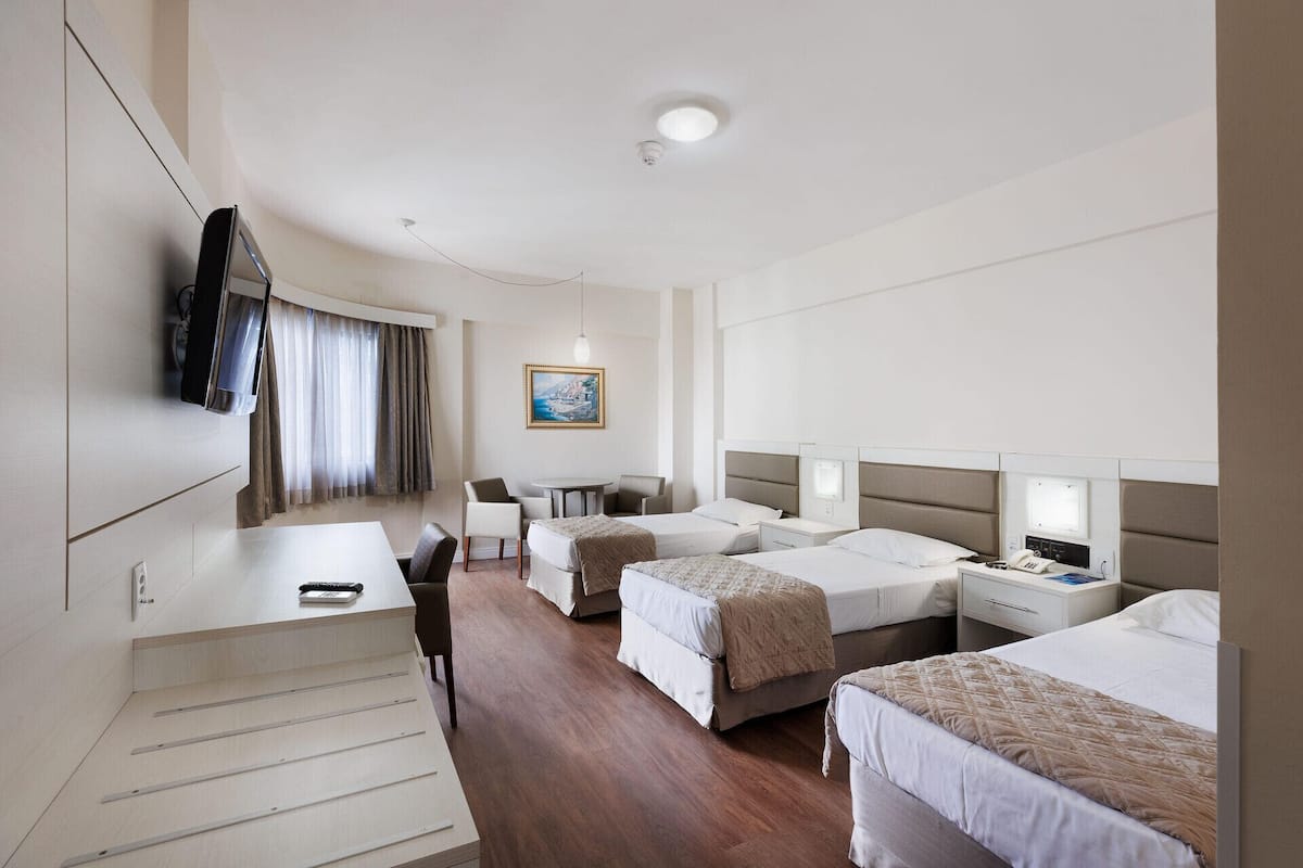 A hotel room with a desk, two beds, a TV, a painting, and a ceiling light.