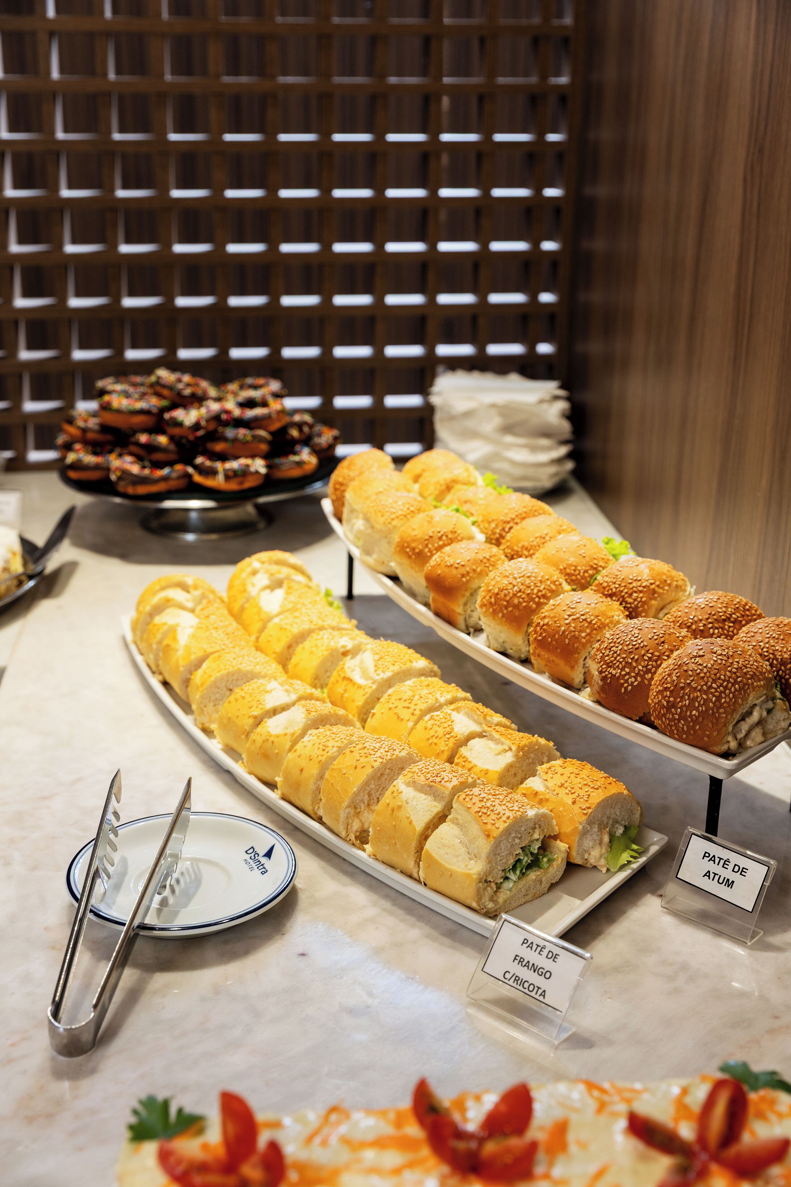 Buffet com diversos alimentos, incluindo sanduíches e doces.