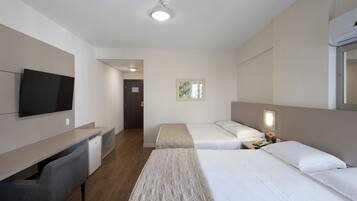 A hotel room with two beds, a desk, a television, and a door leading to another room.