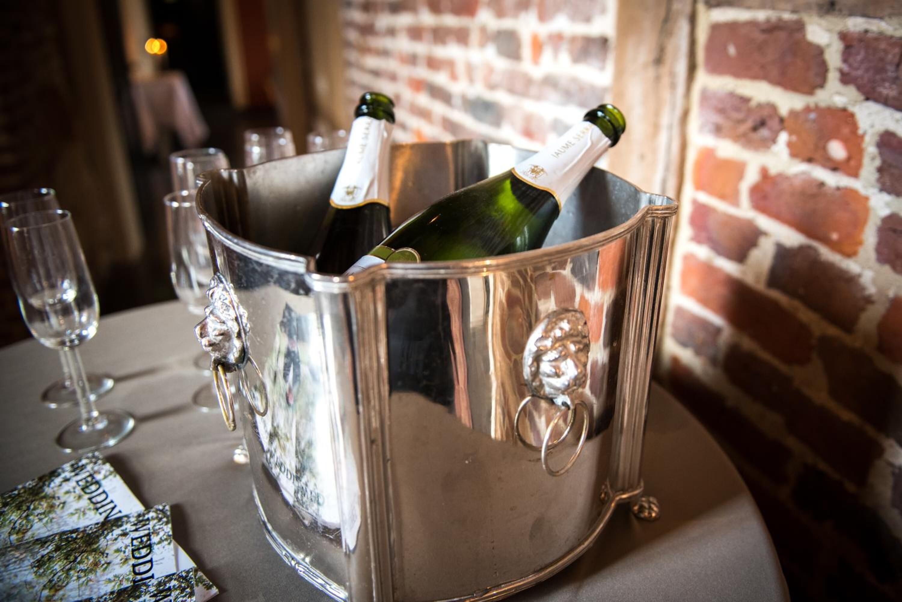 A metallic champagne bucket with two bottles on a table, glasses, and a menu.