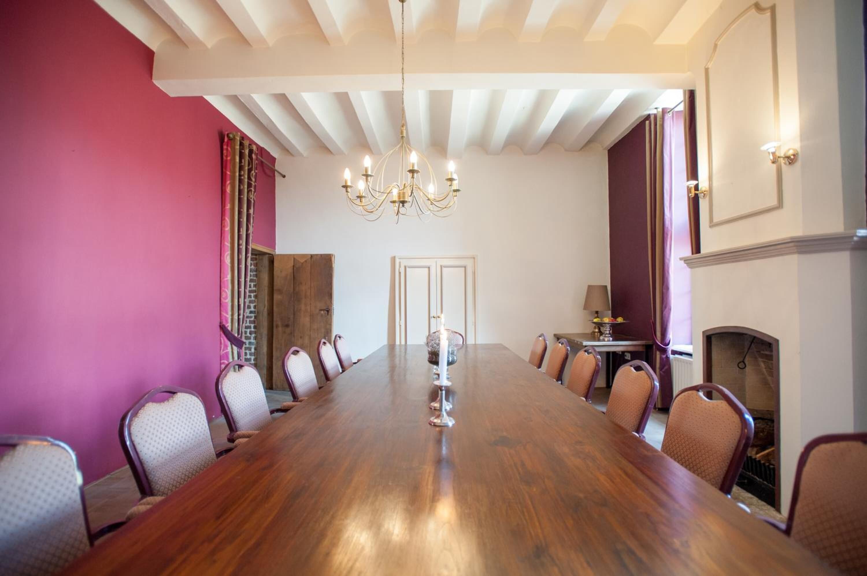 Un salón de conferencias con una larga mesa de madera, sillas, un candelabro y una chimenea.