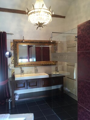 A bathroom with a large mirror, two sinks, a chandelier, and a glass shower enclosure. - Hotel Schinvelder Hoeve (Schinveld)