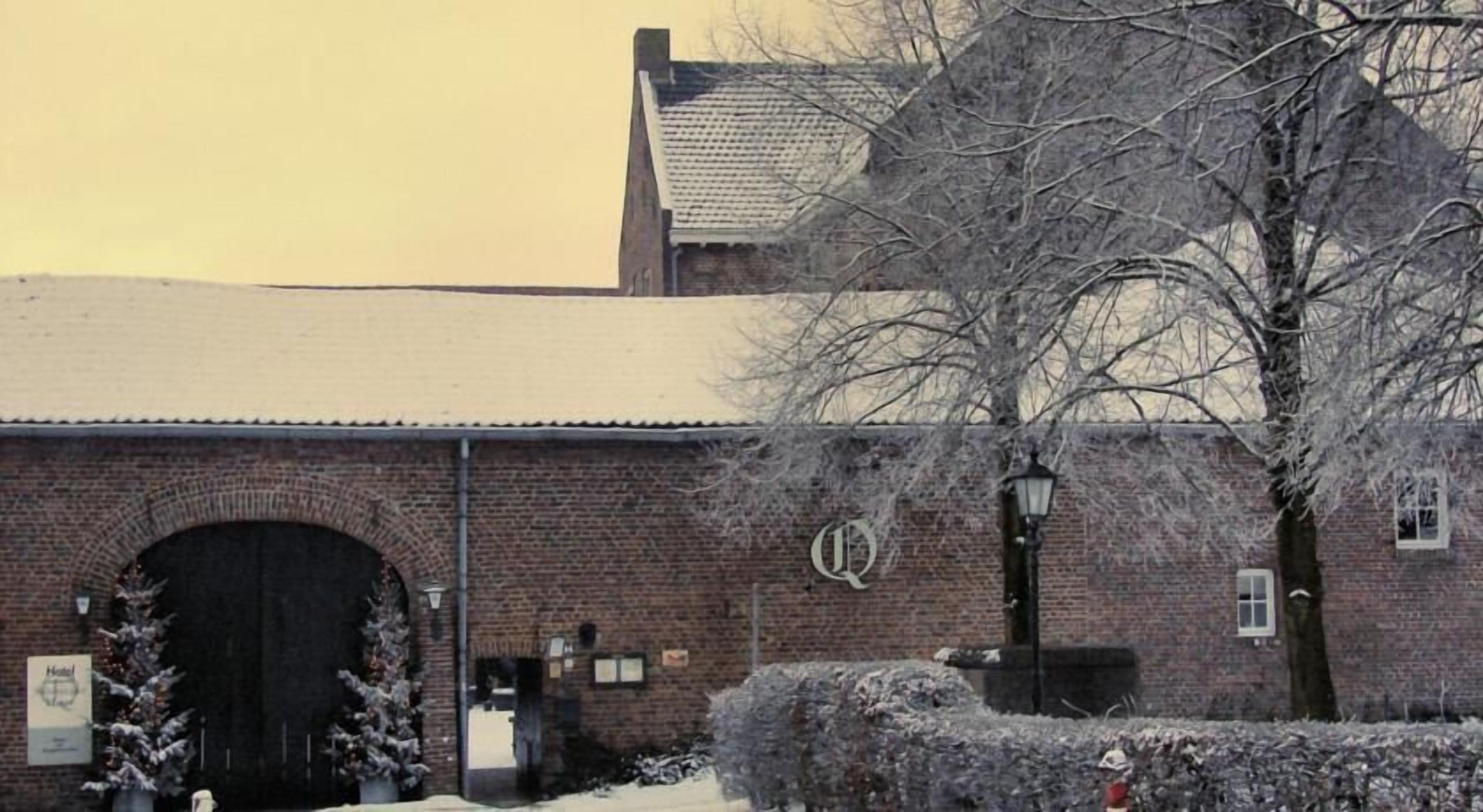 A brick building with a large arched entrance, a sign with a 'Q' logo, and a snow-covered environment.