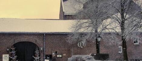 A brick building with a large arched entrance, a sign with a 'Q' logo, and a snow-covered environment.
