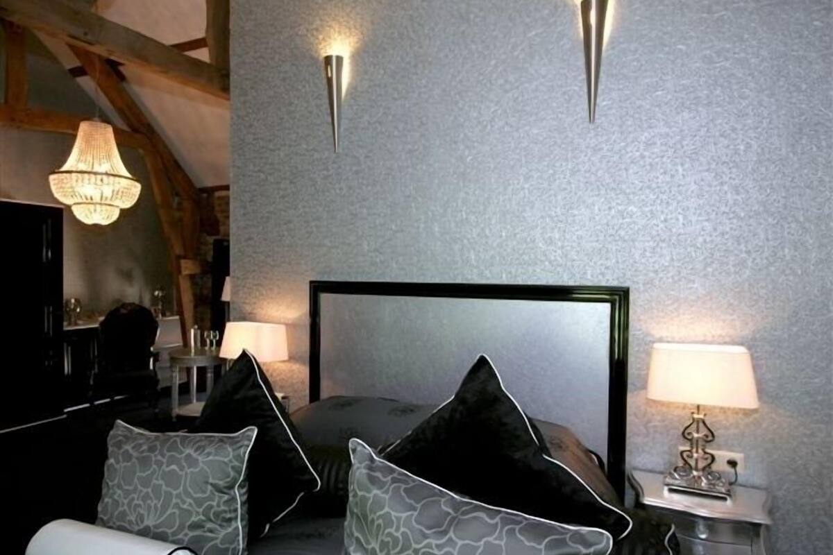 A bedroom with a large bed, two bedside tables, a chandelier, and a textured wall.