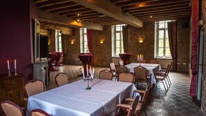 A dining area with tables set for multiple guests, wooden beams on the ceiling, and brick walls.