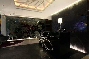 Un moderno vestíbulo de hotel con un mostrador de recepción, zona de estar y paneles decorativos en la pared.