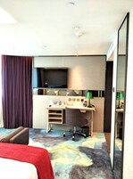 Habitación de hotel con cama, escritorio, silla, televisión y piso alfombrado.