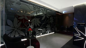 Ein modernes Interieur mit einer Glastrennwand mit floralem Dekor, einem Empfangstresen und einer Sitzecke mit einer Vase roter Blumen.