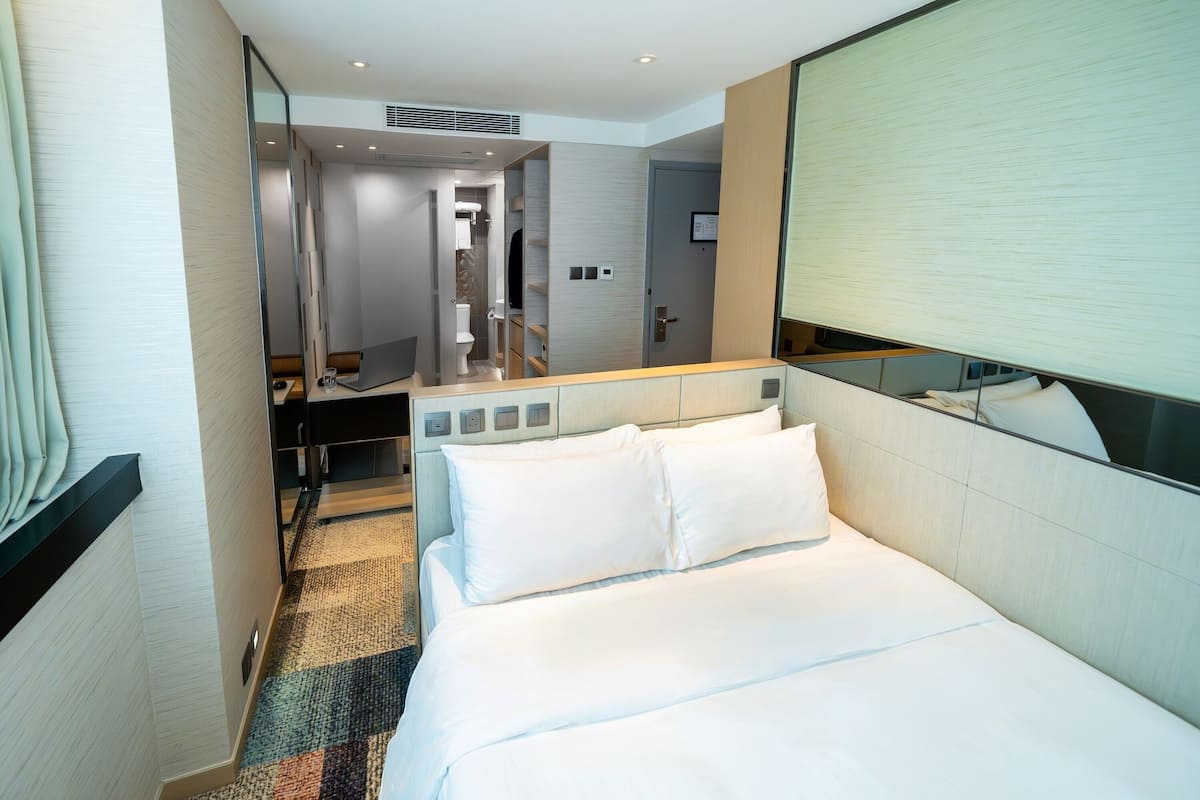 A hotel room with a bed, a desk, a mirror, and a bathroom visible through an open door.