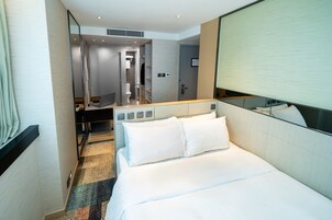 Habitación de hotel con cama, escritorio, espejo y baño visible a través de una puerta abierta.