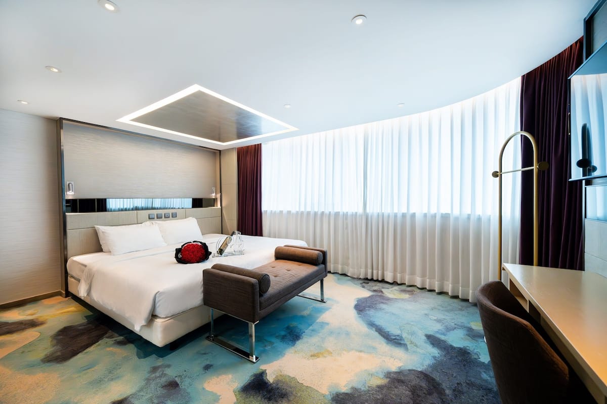 A modern hotel room with a bed, a desk, and a large window with curtains.