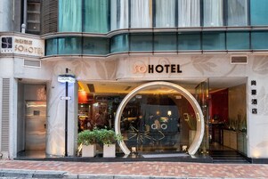Entrada de un hotel con una puerta de vidrio circular, un cartel que dice "SOHOTEL" y un área de acceso con pavimento de ladrillo.