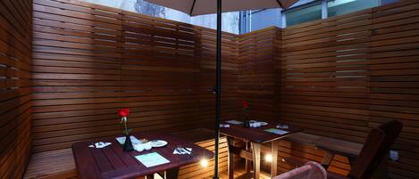 An outdoor patio with wooden furniture, including tables and chairs, under a large umbrella.