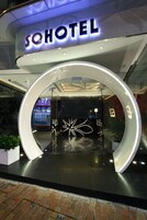 Una entrada de hotel moderna con una puerta de cristal circular, un mostrador de recepción visible y un letrero que dice "SOHOTEL".