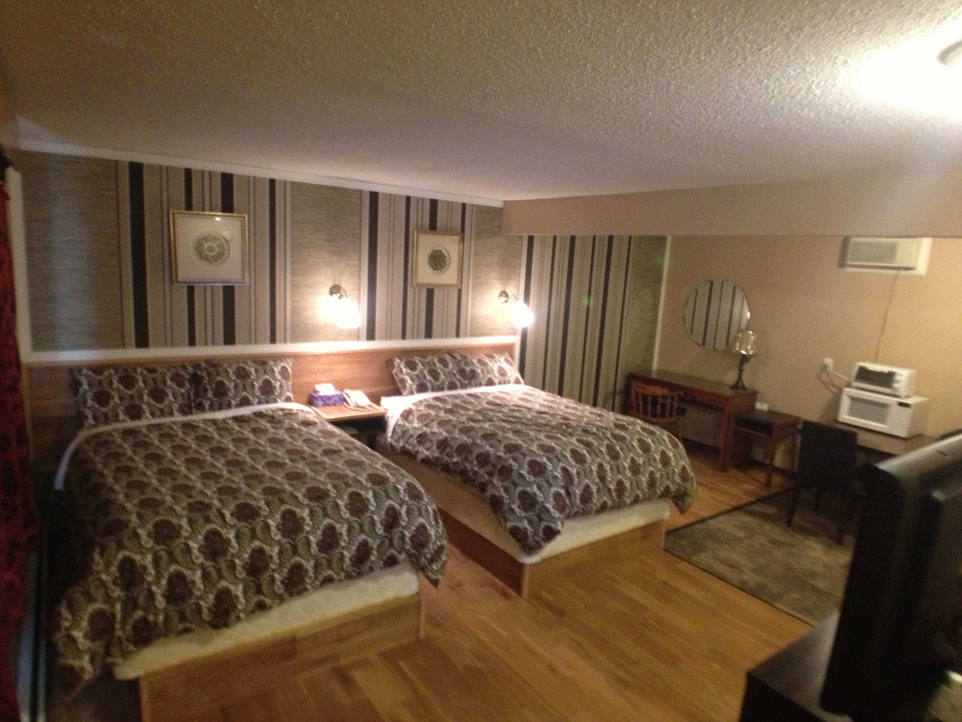 Habitación de hotel con dos camas, un escritorio, una silla, un televisor y un microondas.
