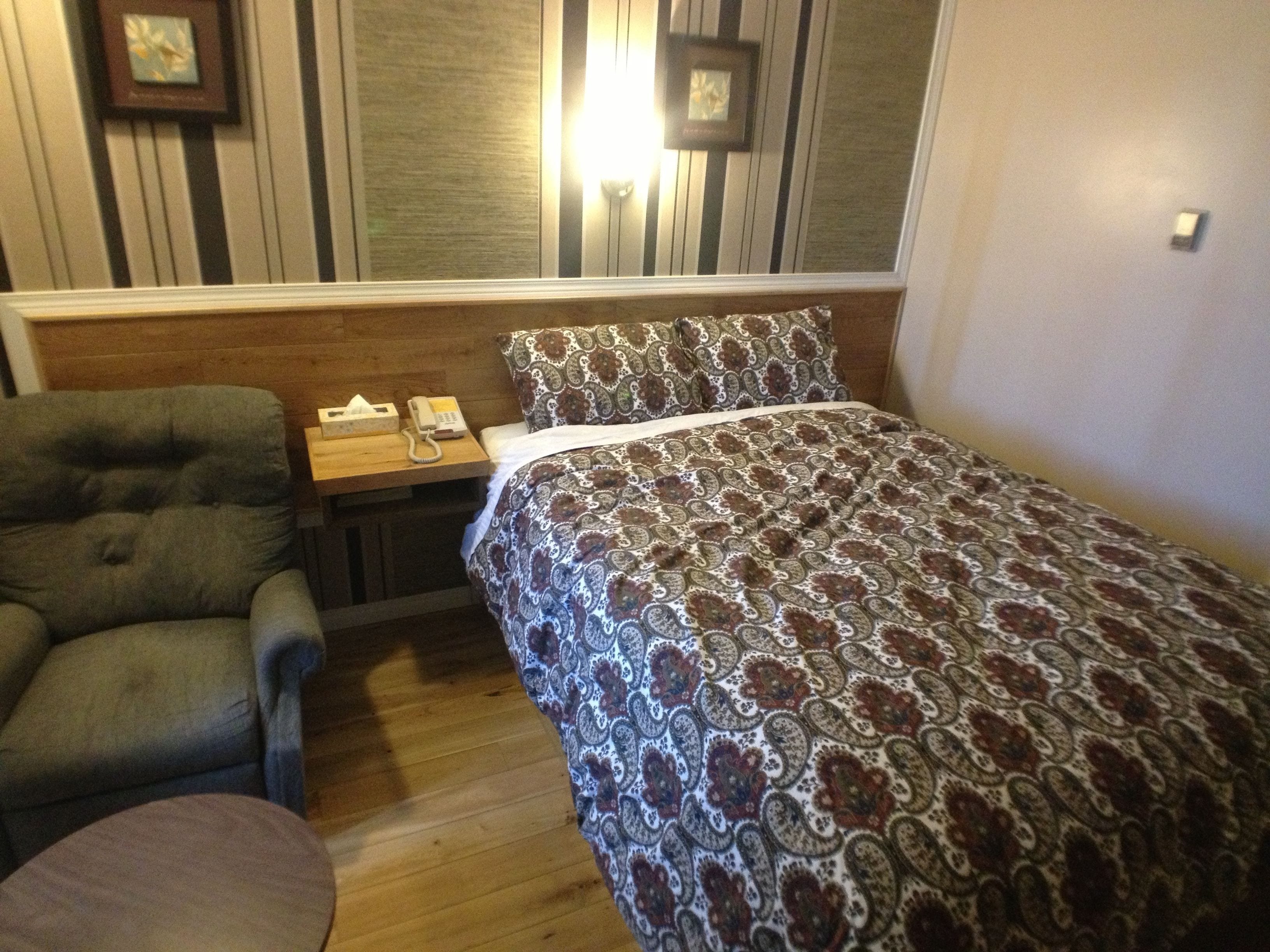 A small, cozy room with a single bed, a chair, and a bedside table with a telephone.