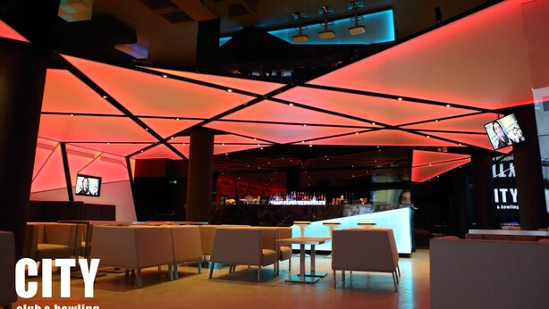 Un moderno espacio lounge con asientos y bar, que destaca por diseños geométricos en el techo e iluminación ambiental.
