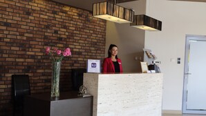 Un mostrador de recepción con un fondo de pared de ladrillo, un jarrón de flores rosadas y una lámpara moderna.