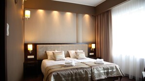 Una habitación de hotel con una cama grande, dos lámparas de noche y una ventana con cortinas.