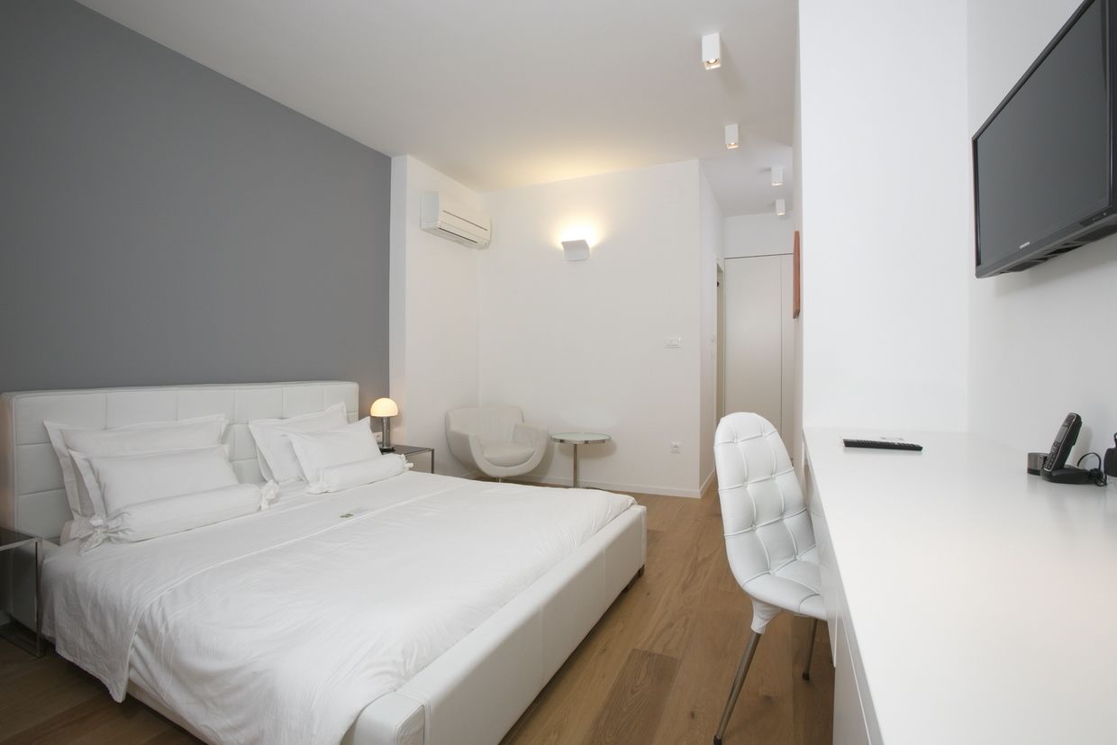 A modern hotel room with a large bed, a desk, a chair, a TV, and a small table.