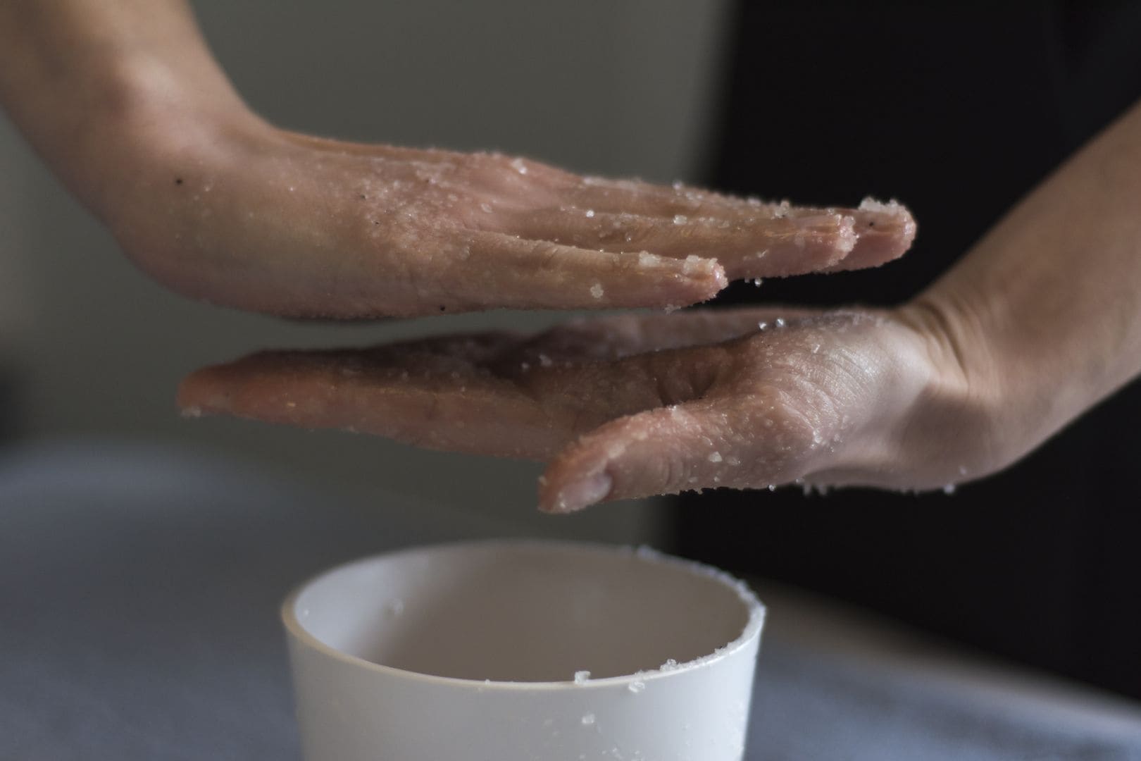 Nahaufnahme von Händen, die Salz in eine weiße Tasse streuen.