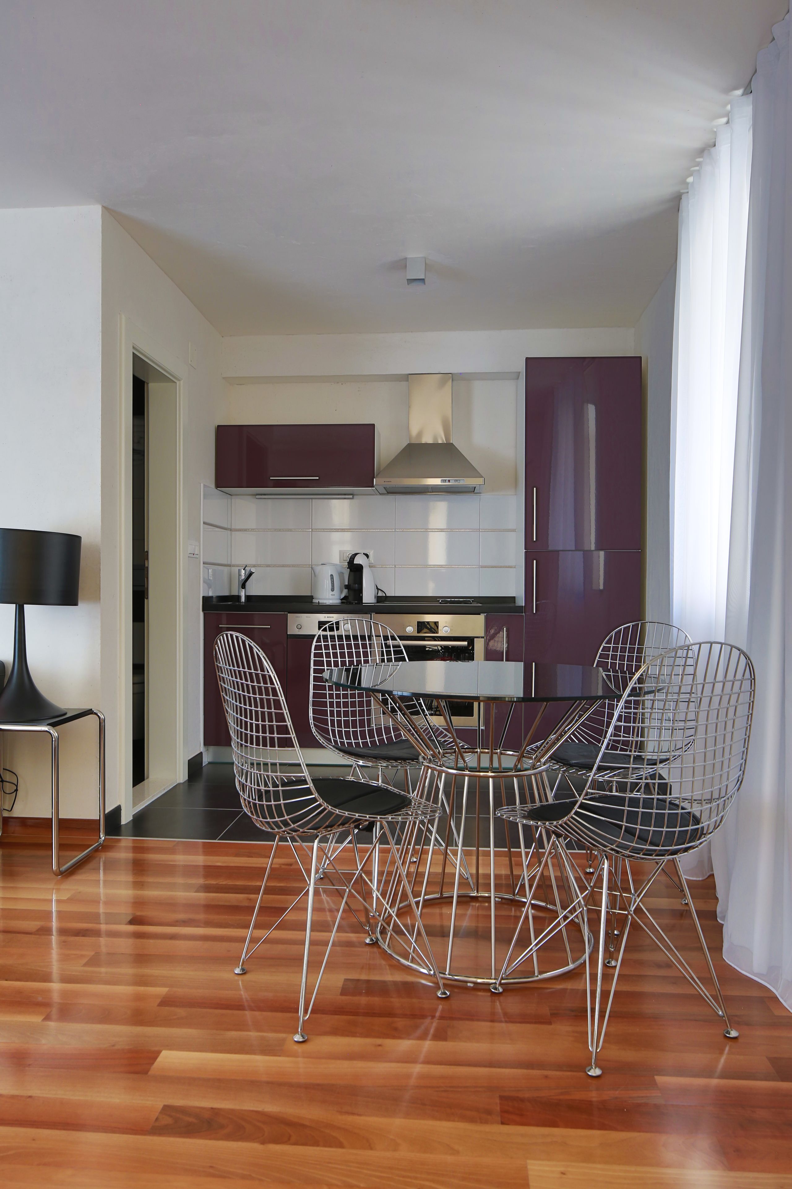 Une cuisine moderne avec un coin repas, comprenant une table entourée de chaises au design épuré, une lampe noire et un plancher en bois.